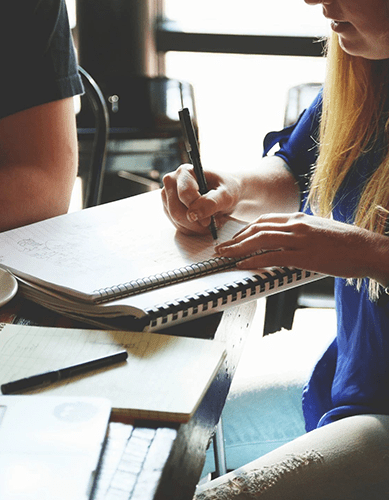 A person writing on a notebook at a table.