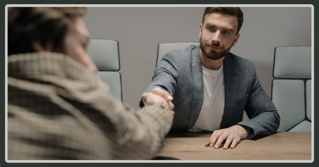 Two men shaking hands across a conference table, signifying a successful resolution or agreement after a discussion.