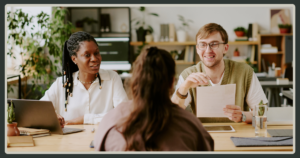 Two smiling interviewers, a Black woman and a man with glasses, review a candidate’s resume during a professional job interview.