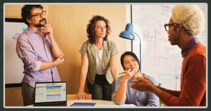 A diverse team of four colleagues engages in a brainstorming session around a table with a laptop and whiteboard in a bright office.
