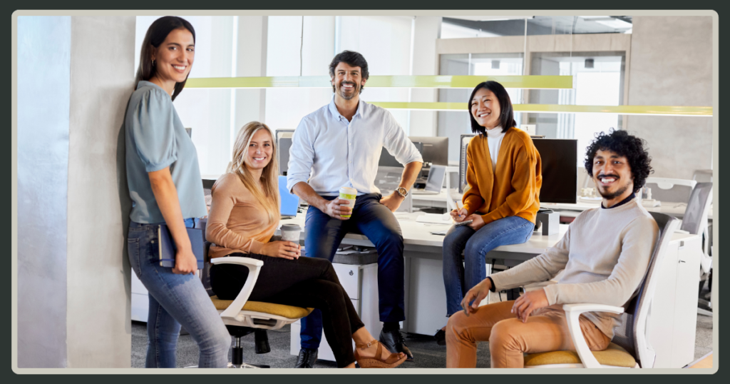 A diverse group of five smiling colleagues posing together in a bright, modern office, conveying a sense of community and trust.