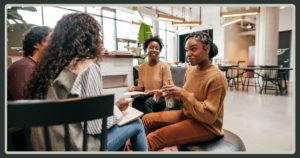 A group of diverse professionals sitting in a circle in a bright, modern office lounge, engaged in a collaborative and informal team discussion.
