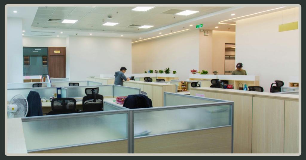 A wide-angle view of a bright, modern open-plan office featuring several rows of clean, light-colored cubicles and workstations.