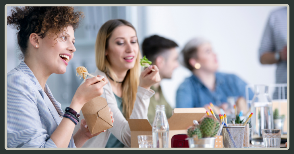 A diverse group of office workers enjoying a healthy takeout lunch together at a long table during a casual midday session.