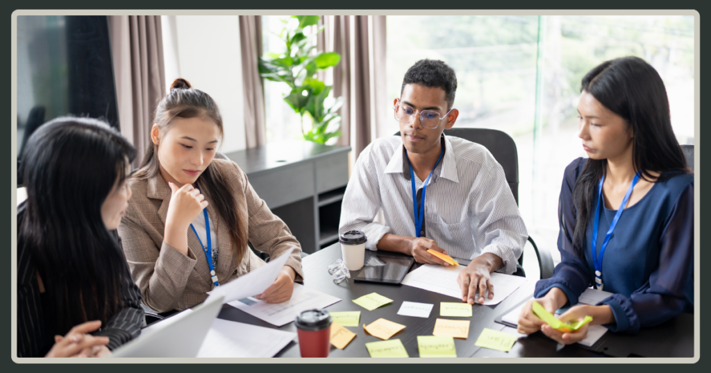 A diverse team of four colleagues gathered around a conference table covered in colorful sticky notes and documents for a planning session.