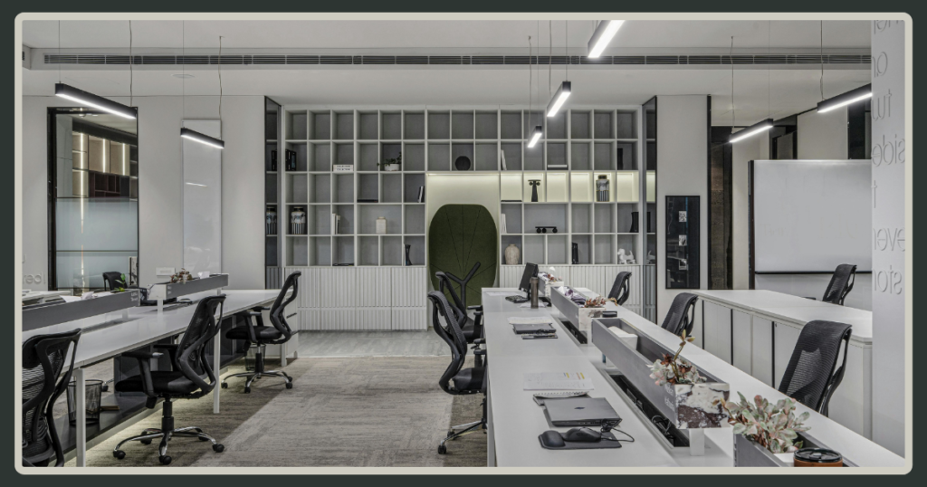 A wide, symmetrical view of a sleek, minimalist open-plan office with white desks, ergonomic black chairs, and a large architectural bookshelf.